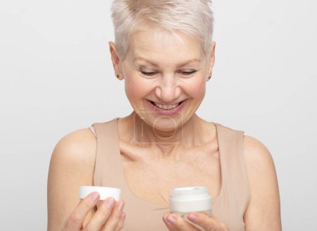 Photo for An elderly woman holds a jar of cream, opens it, smiles. The concept of self-care, beauty at any age. - Royalty Free Image