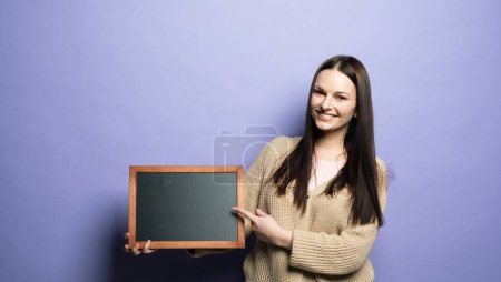 Photo for Young smiling student woman holding a chalkboard isolated on purple background. - Royalty Free Image