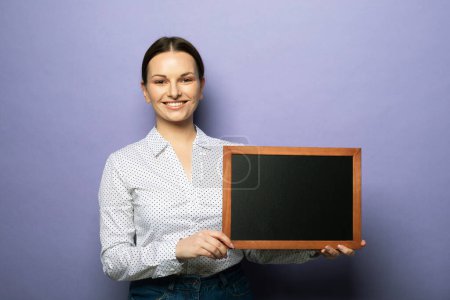 Téléchargez les photos : Young smiling woman holding a chalkboard isolated on purple background. - en image libre de droit