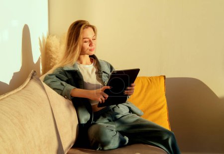 Téléchargez les photos : Camera approaching joyful young caucasian beautiful woman sitting in apartment on sofa with tablet pc surfing internet, studying or working at home, social network user, leisure concept - en image libre de droit