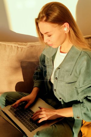 Photo for Camera approaching joyful young caucasian beautiful woman sitting in apartment on sofa typing on laptop surfing internet, studying or working at home, social network user, leisure concept - Royalty Free Image