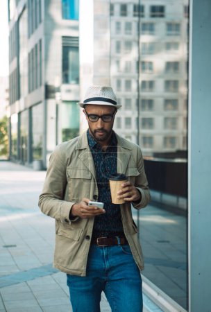 Photo for Young man in white hat walk hold mobile cell phone takeaway delivery cup coffee. Street. Summer. Lifestyle concept. - Royalty Free Image