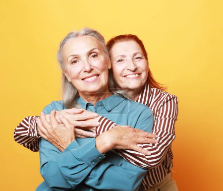 Foto de Two happiness elderly women friends hugging on yellow background. Lifestyle, friendship and old people concept. - Imagen libre de derechos