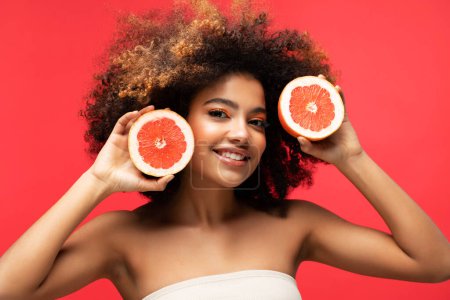Téléchargez les photos : Photo of young dark skin female with grape, isolated on red color background. Close up portrait. - en image libre de droit