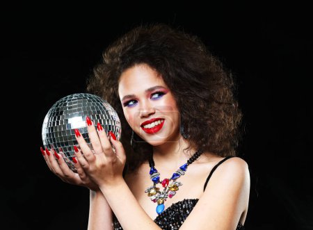 Foto de Portrait of young beautiful african woman with bright make up holding disco ball over black background, close up portrait - Imagen libre de derechos