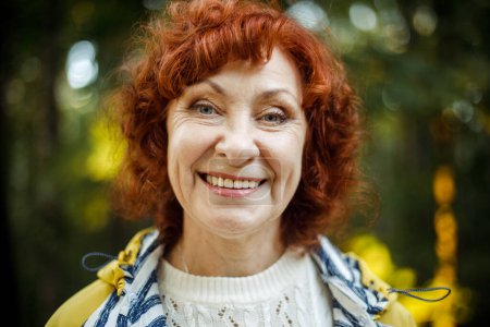 Photo for Portrait of a happy laughing elderly woman with red curly hair in the autumn park. - Royalty Free Image