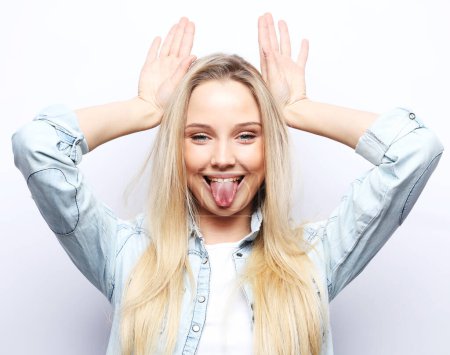 Foto de Lifestyle, emotion and body language concept: Young blonde woman wearing casual doing funny gesture with finger over head as bull horns - Imagen libre de derechos