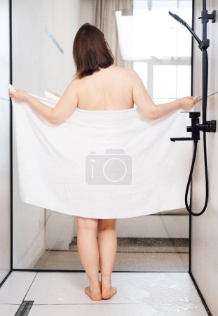 Photo for Chubby young woman in the shower room drying off and wrapping herself in a white towel - Royalty Free Image