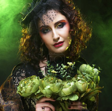 Téléchargez les photos : Beautiful woman with bright creative make up holding dry flowers, close up portrait over green color background. - en image libre de droit