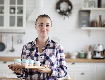 Téléchargez les photos : Young baker woman holding marshmallow. Happy, smiling and cheerful. Freelance, food and hobby concept. - en image libre de droit