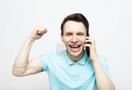 Photo for Happy young man in shirt gesturing and smiling while talking on the mobile phone, portrait over white background - Royalty Free Image