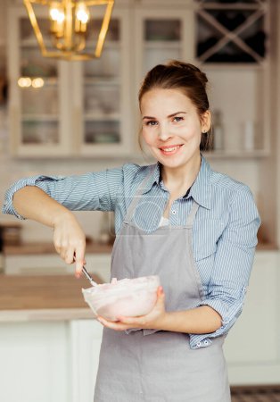 Foto de Young smiling woman mixes cake cream using a spatula - Imagen libre de derechos