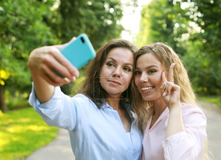 Photo for Lifestyle, family and people concept: mature mother and adult daughter are doing selfie by mobile phone in summer park - Royalty Free Image