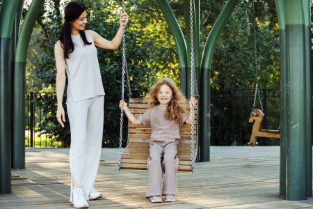 Téléchargez les photos : Portrait of enjoy happy love mother with little child girl smiling playing and pushing daughter on the swing moments good time in park - en image libre de droit