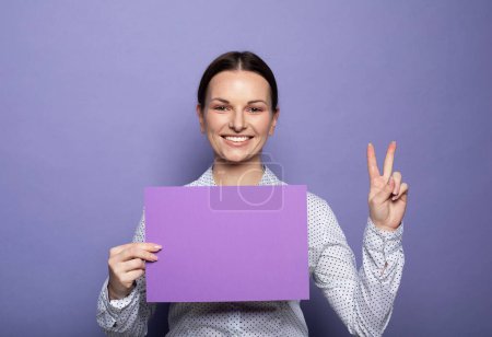 Photo for Young brunette woman holding purple blank advertising board standing on lilac background in studio - Royalty Free Image