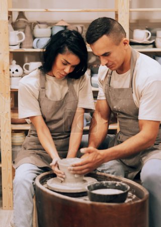 Téléchargez les photos : A young lovely couple creates a vase on a potter's wheel in a ceramic workshop. The concept of hobby and creativity. - en image libre de droit