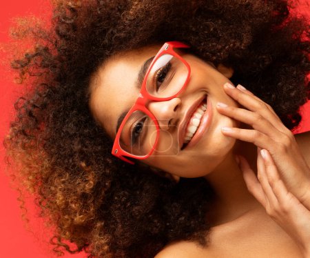 Photo for Happy woman wearing eyeglasses smiling, has good mood isolated on studio red background. Excited african american female. Positive life concept. - Royalty Free Image