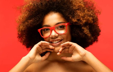 Photo for Portrait of smiling beautiful african american young woman. Model female with afro wearing eyeglasses. Red background. - Royalty Free Image