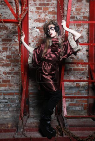 Téléchargez les photos : Jeune femme avec un maquillage lumineux dans un décor steampunk tient avec ses mains pour les chaînes rouges. - en image libre de droit