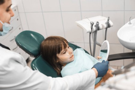 Foto de People, medicine, stomatology, technology and health care concept. Professional young male dentist working with little girl in clinic. - Imagen libre de derechos