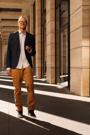 Téléchargez les photos : Style de vie, affaires et concept de personnes : Jeune élégant bel homme habillé casual passer à côté des colonnes d'un grand bâtiment moderne - en image libre de droit