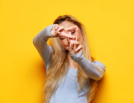 Foto de Lifestyle, emotion and young people concept: Young blonde woman smiling and show v-sign over yellow background - Imagen libre de derechos