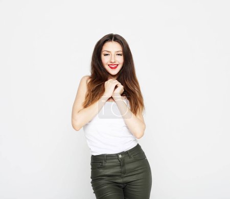 Téléchargez les photos : Lifestyle, emotion and young people concept: charming smiling young woman with long dark hair dressed in a white t-shirt and jeans over white background - en image libre de droit