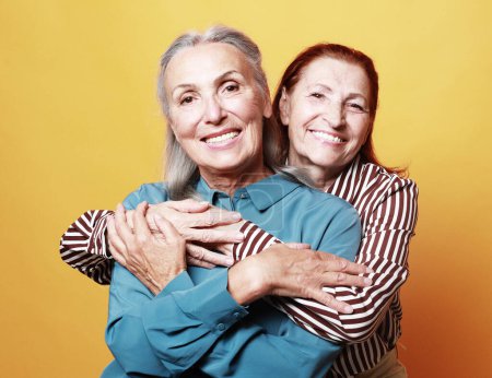 Téléchargez les photos : Two smiling elderly women friends hugging on yellow background. Lifestyle, friendship and old people concept. - en image libre de droit