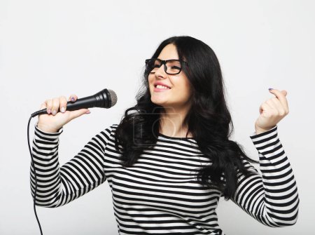 Téléchargez les photos : Jeune chanteuse brune courbée avec un microphone sur fond gris clair - en image libre de droit