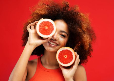Foto de Photo of young dark skin female model with grape, isolated on red color background - Imagen libre de derechos