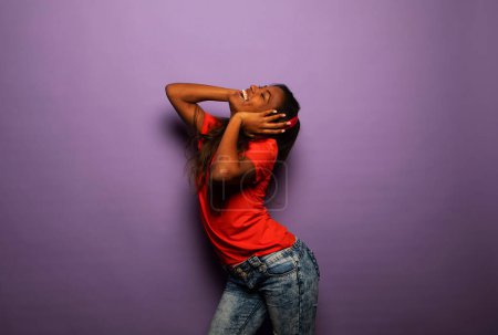 Téléchargez les photos : Enthousiaste mélange race femme avec les cheveux longs écouter de la musique préférée par écouteurs sur fond violet - en image libre de droit