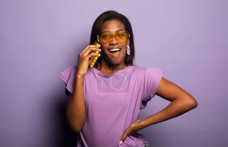 Téléchargez les photos : Photo de jeune femme noire heureux sourire positif parcourir le téléphone portable sur fond violet - en image libre de droit