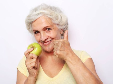 Foto de Elegante vieja mujer sonriente con pelo blanco sosteniendo manzana verde sobre fondo blanco - Imagen libre de derechos