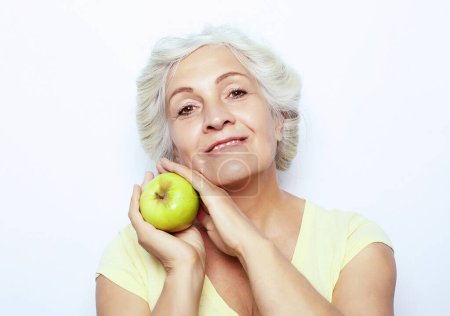 Photo for Elegant old smiling woman with white hair holding green apple over white background - Royalty Free Image