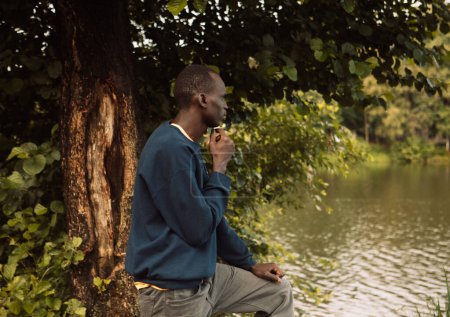 Téléchargez les photos : A young black man is looking at the lake. Morning. Summer day. - en image libre de droit