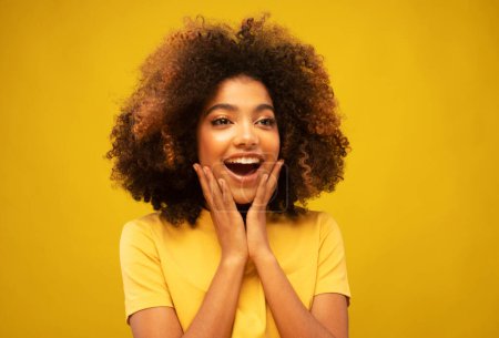 Photo for Young African Woman Surprised Smiling at Camera on Yellow Background. Young Female Holds Hands Near Her Face and Smiles Widely. Beauty Concept. - Royalty Free Image