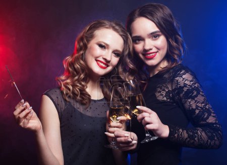 Téléchargez les photos : Deux jolies amies de beauté tenant des étincelles et souriant en regardant la caméra, temps de fête - en image libre de droit