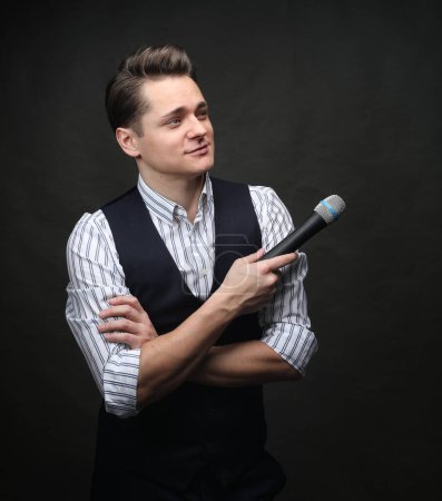 Foto de Joven con estilo sosteniendo un micrófono, posando sobre un fondo oscuro con humo, actor, cantante, espectáculo, anfitrión del evento. - Imagen libre de derechos