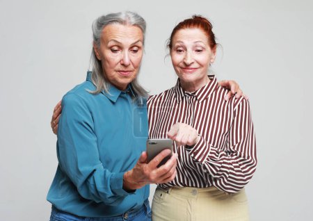 Foto de Dos ancianas miran el teléfono y leen las noticias sobre el fondo gris - Imagen libre de derechos