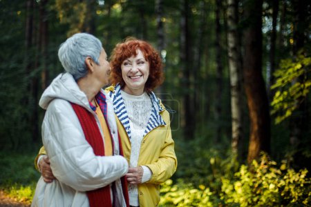 Foto de Feliz pareja de mujeres mayores mirándose caminando en el bosque tomados de la mano. - Imagen libre de derechos