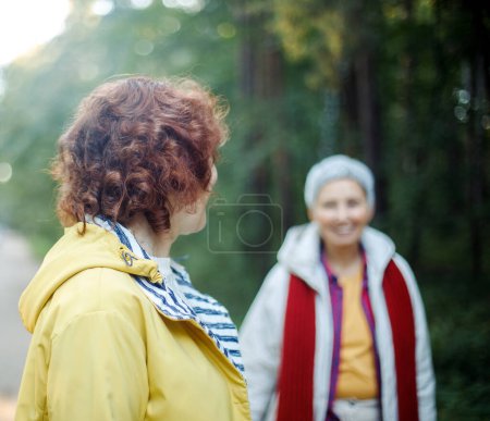 Photo for Cheerful pensioner female friends tallking and laughing in the autumn park. Lifestyle cocnept. - Royalty Free Image