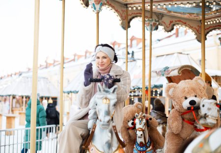 Photo for Pretty woman saddled a horse on a carousel. Christmas market, happiness and fun. - Royalty Free Image