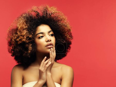 Foto de Young beautiful african american woman with afro hair. Glamour makeup. Red Background - Imagen libre de derechos
