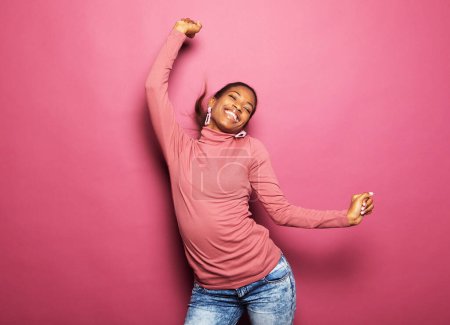Téléchargez les photos : Jeune afro heureux femme porter des vêtements décontractés danse recherche vide espace isolé couleur rose fond - en image libre de droit