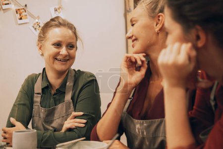 Téléchargez les photos : Trois souriantes jeunes amies joyeuses s'amusent dans un atelier de céramique. - en image libre de droit