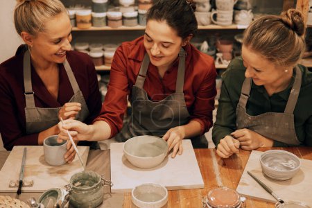 Foto de Una compañía de tres guapas amigas jóvenes hacen tazas de cerámica en un taller de cerámica. Diviértete haciendo arte. - Imagen libre de derechos