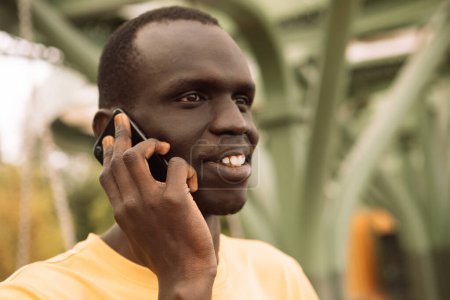 Téléchargez les photos : Un homme noir sérieux appelant sur un téléphone intelligent debout au parc. Saison estivale. - en image libre de droit