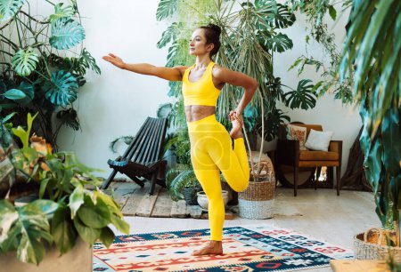 Téléchargez les photos : Une femme pratique le yoga dans la jungle urbaine. Femme en yoga asanas et Pilates à la maison. Concept de style de vie. - en image libre de droit