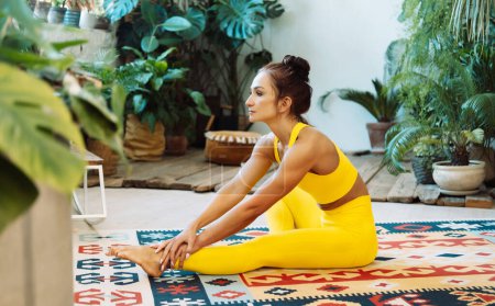 Téléchargez les photos : Brunette femme pratique le yoga à la maison parmi les fleurs. Jungle urbaine et gymnastique, yoga, concept pilates. - en image libre de droit