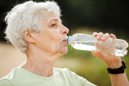 Téléchargez les photos : Femme âgée aux cheveux gris courts buvant de l'eau après l'exercice, portrait dans le parc d'été - en image libre de droit